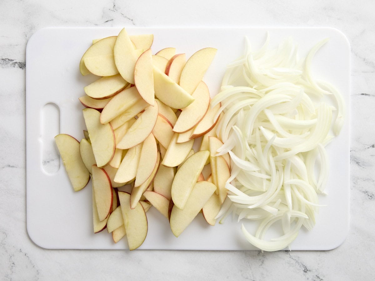 Pommes et oignons tranchés sur une planche à découper blanche.