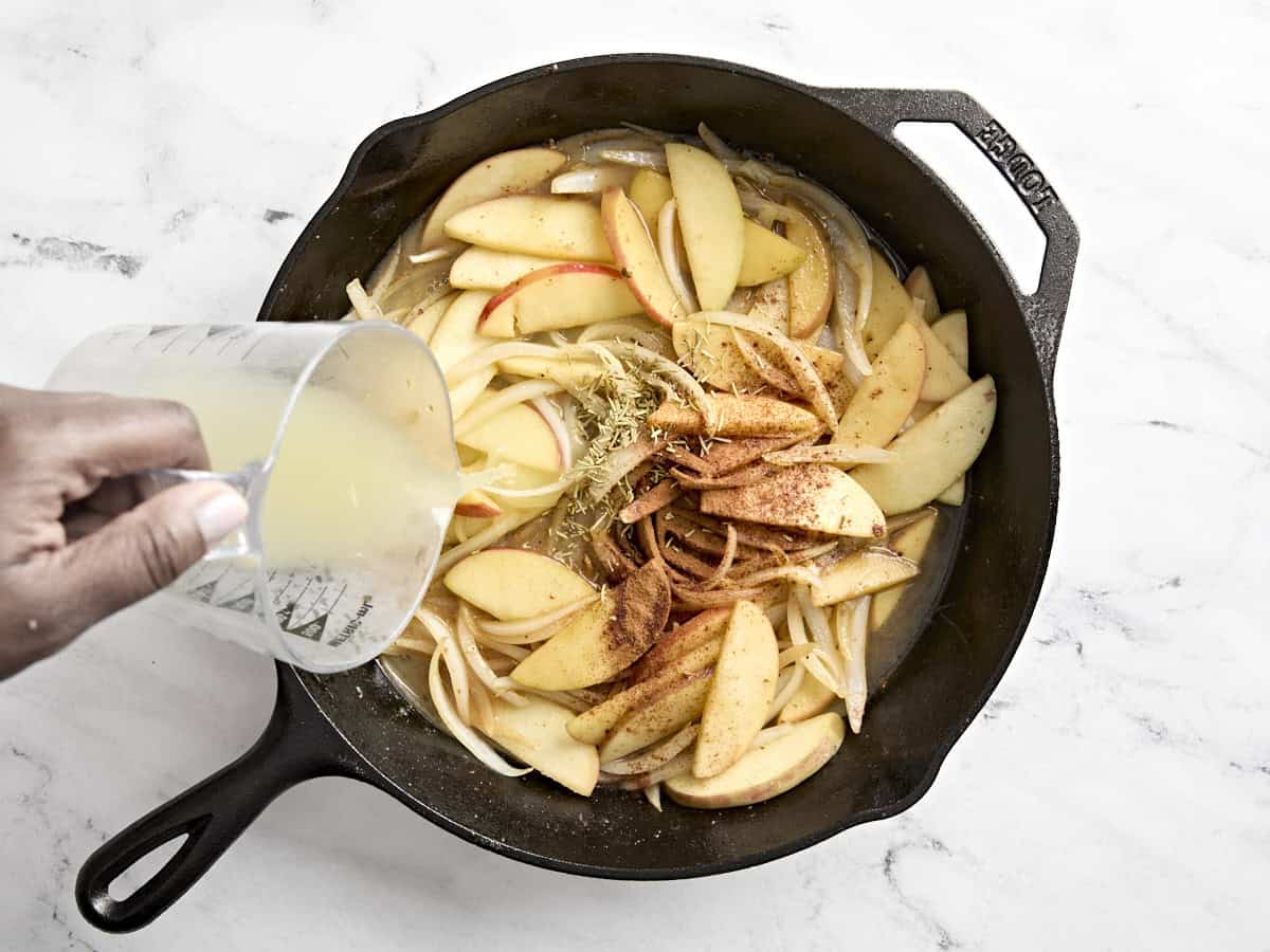 Bouillon de poulet et versé dans une poêle avec les assaisonnements et les tranches de pommes et d'oignons.