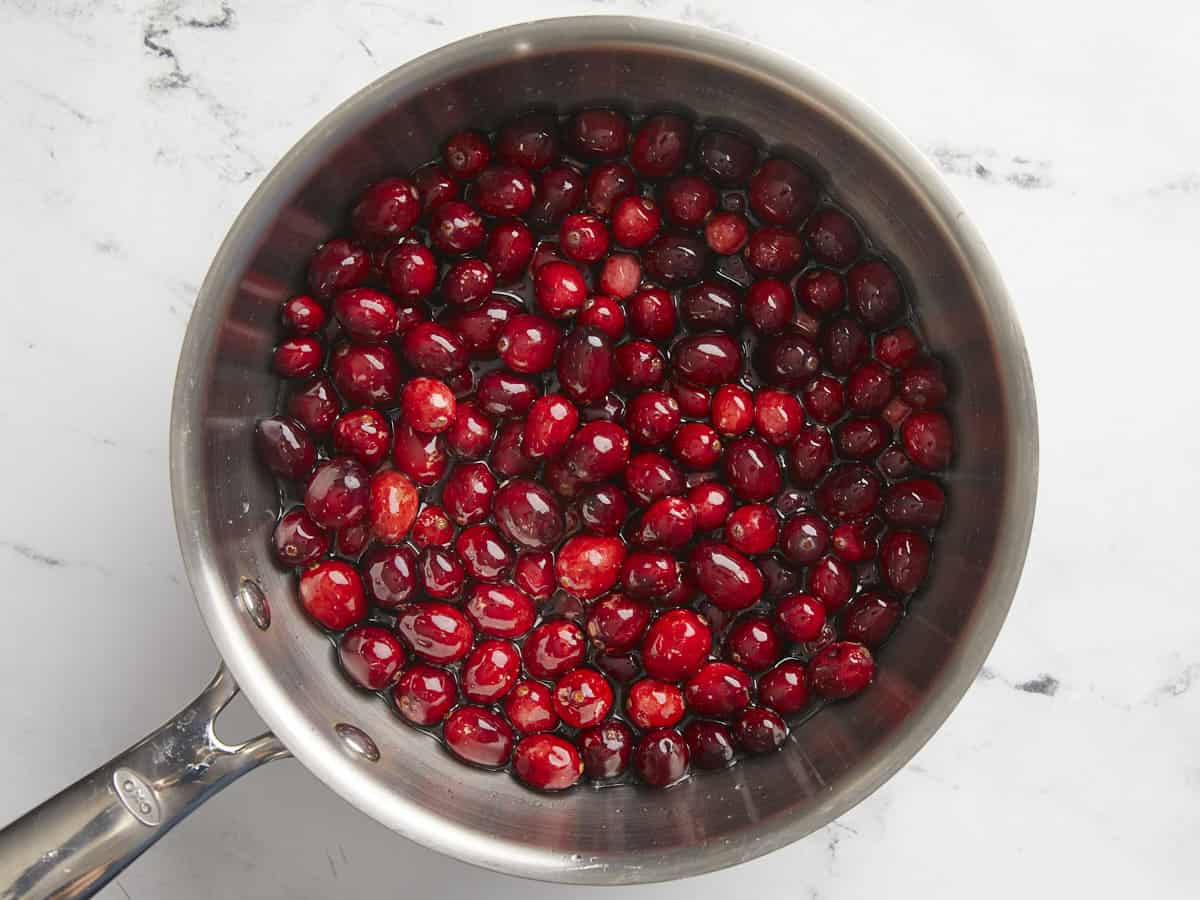 Canneberges fraîches ajoutées à la casserole avec l'eau et le sucre.
