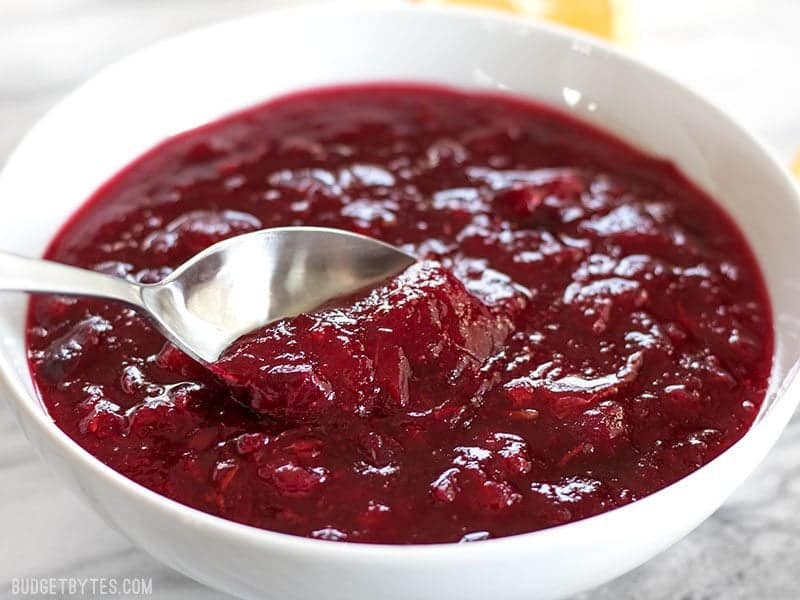 Cette simple sauce aux canneberges classique ne nécessite que trois ingrédients mais a suffisamment de saveur pour ajouter du piquant à votre repas des Fêtes. Budgetbytes.com Un bol de sauce aux canneberges épaisse prête à être servie sur votre table de fêtes