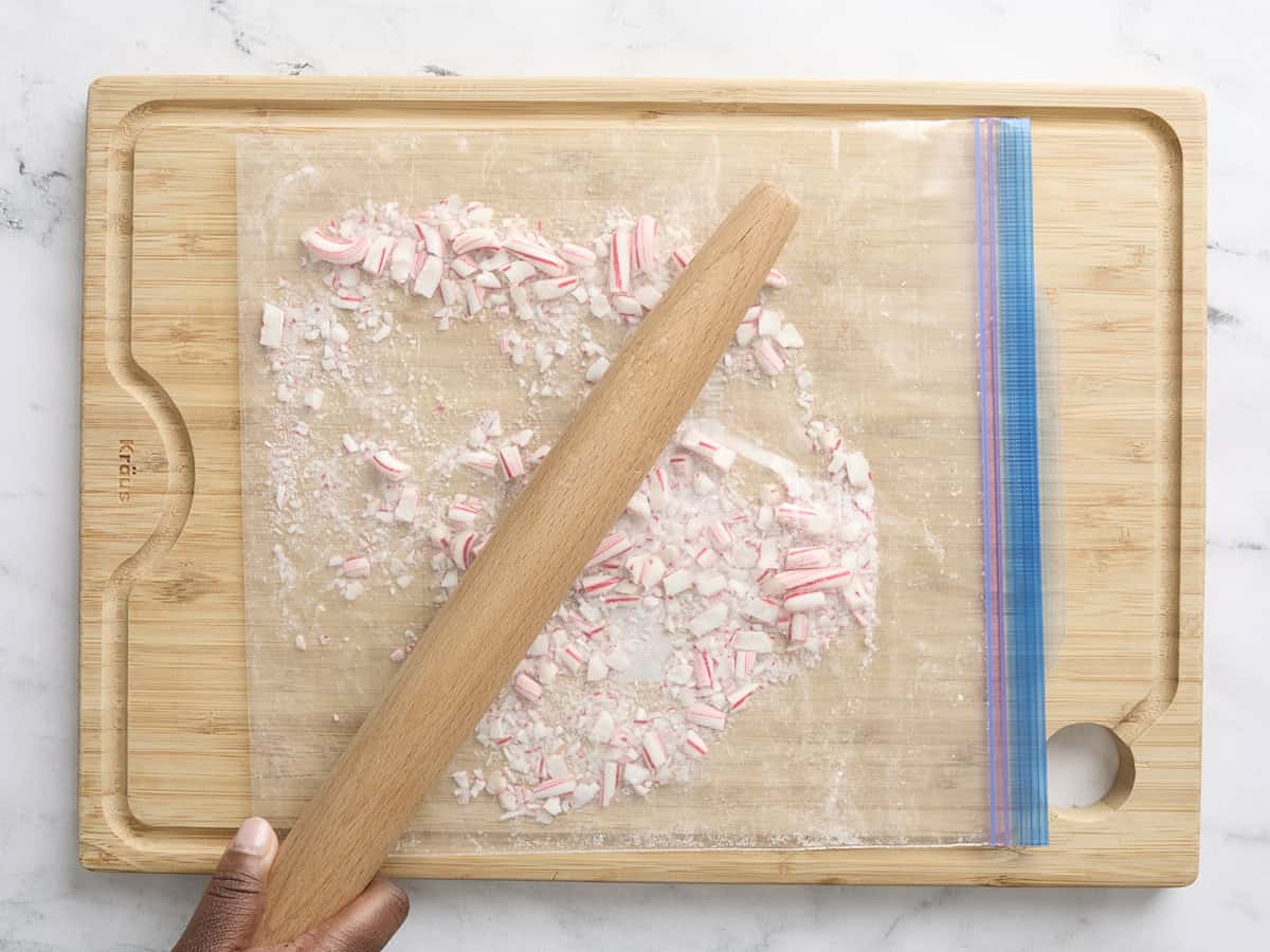 Un rouleau à pâtisserie écrasant des cannes de bonbon dans un sac de conservation des aliments.