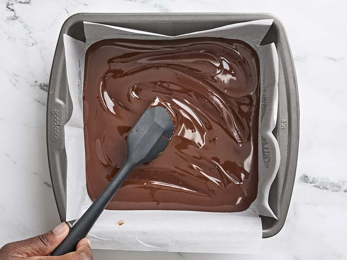 Une spatule étalant le chocolat fondu sur une plaque à pâtisserie tapissée de papier sulfurisé.