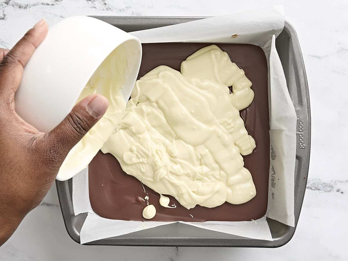 Chocolat fondu versé sur du chocolat mi-sucré dans un plat allant au four tapissé de papier sulfurisé pour faire de l'écorce de menthe poivrée.