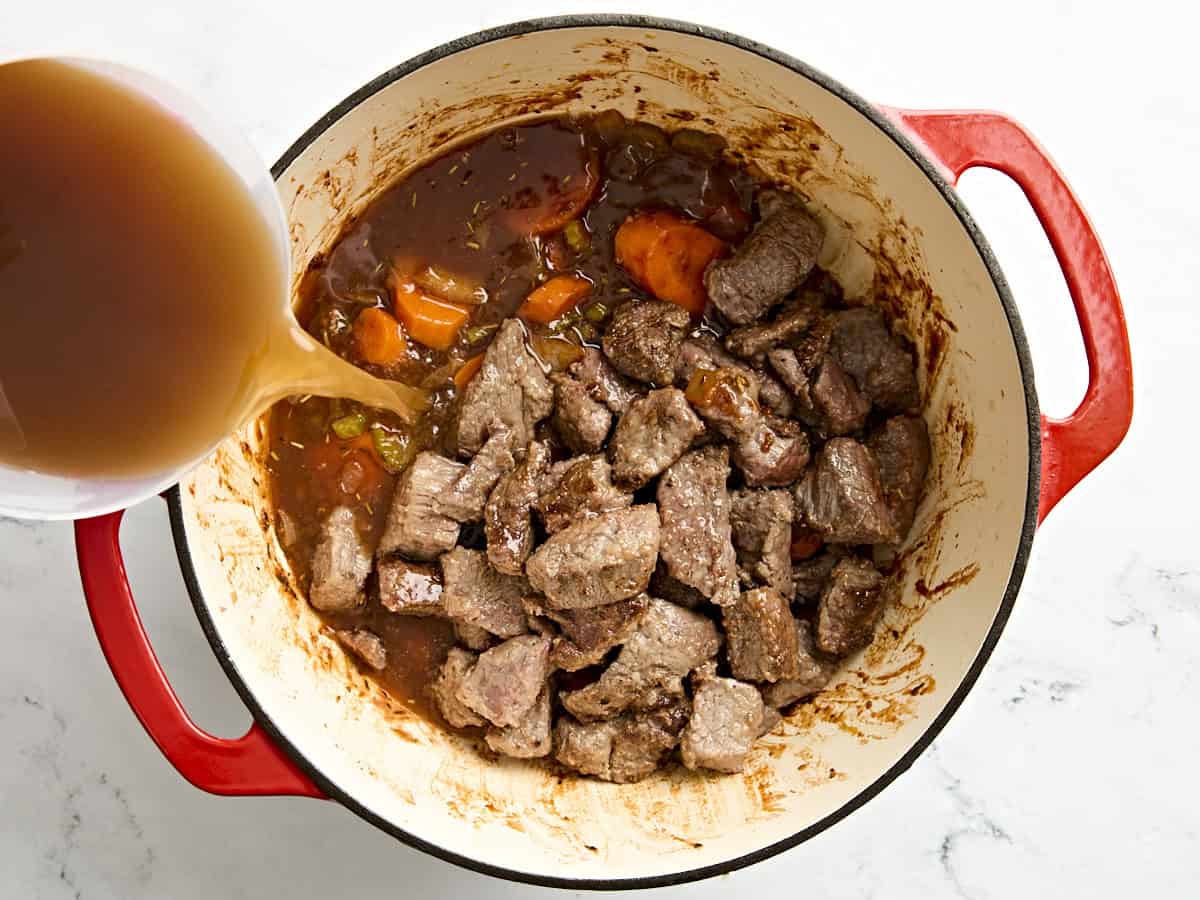 Bouillon versé sur un ragoût de bœuf dans une cocotte.