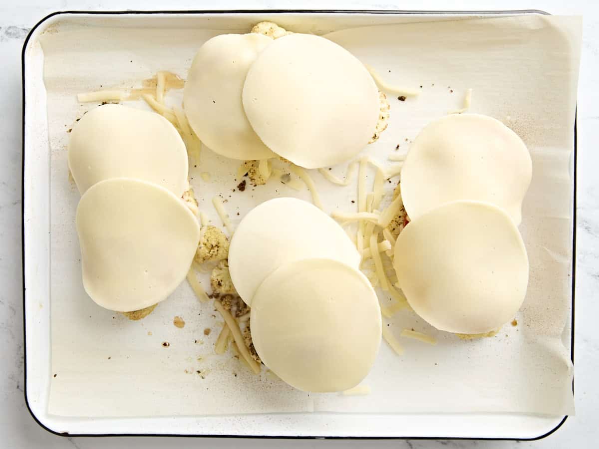 Tranches de fromage provolone ajoutées au chou-fleur parmesan sur une plaque à pâtisserie tapissée de papier sulfurisé.