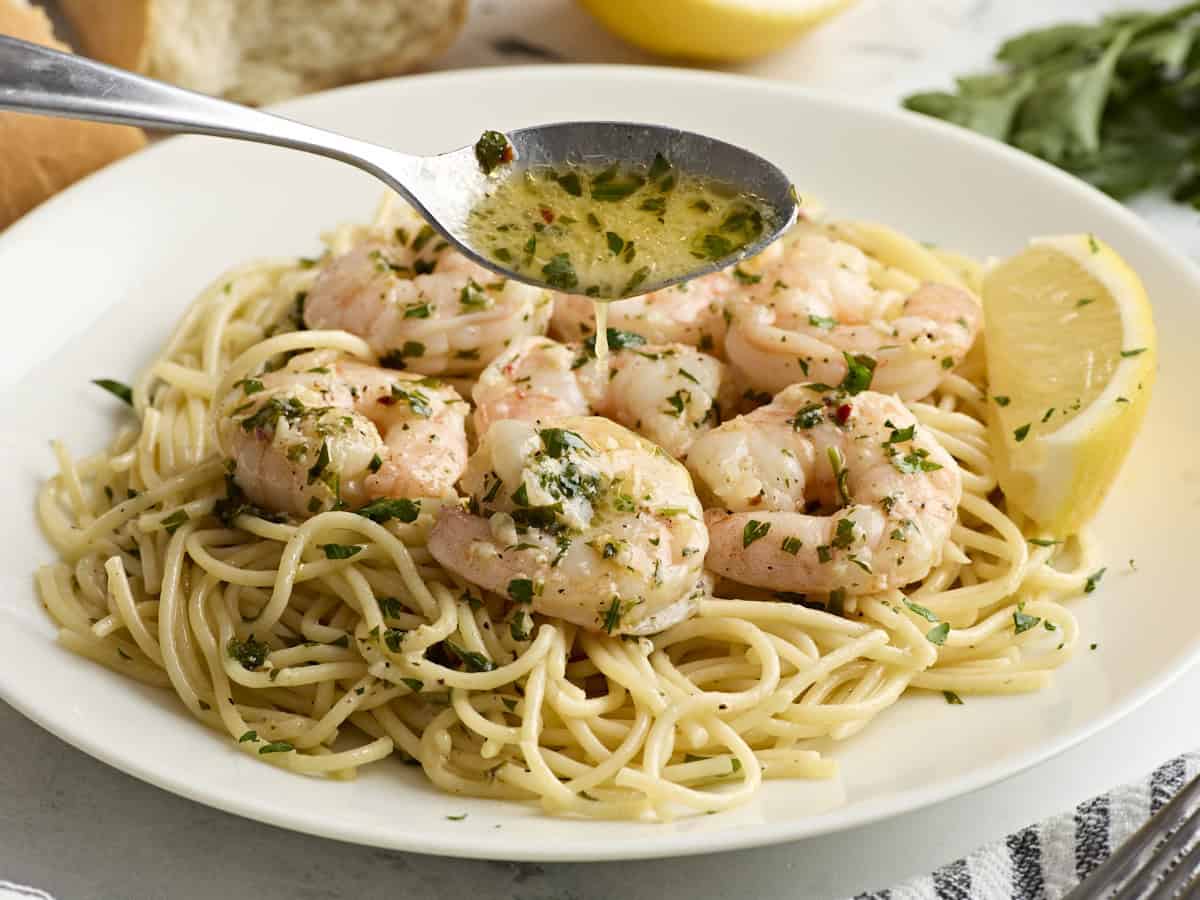 Une cuillère versant la sauce au beurre à l'ail sur les langoustines aux crevettes et les spaghettis.