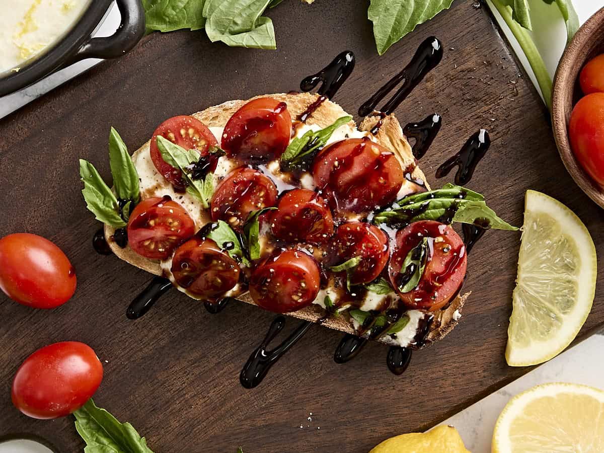 Vue aérienne de pain grillé à la ricotta avec tomates grillées, basilic et réduction balsamique.