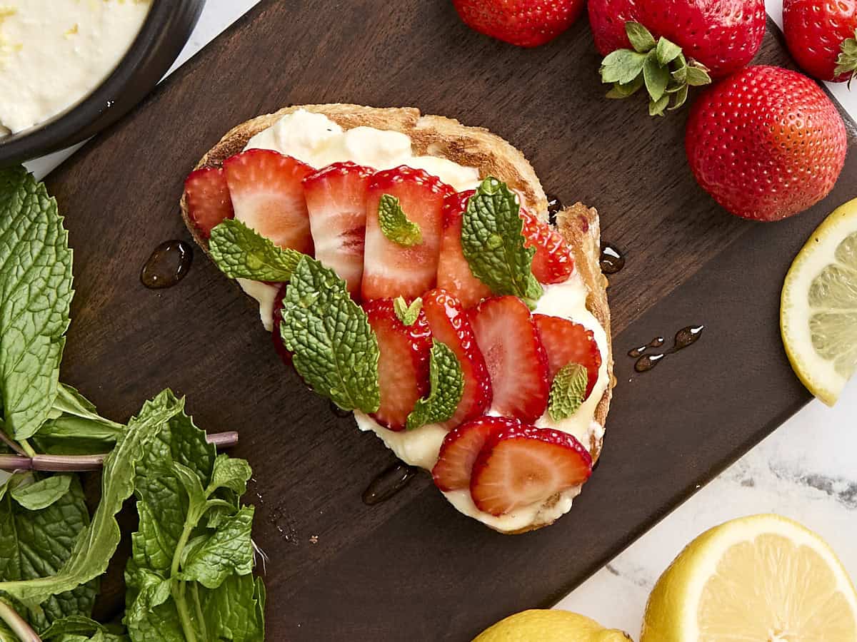 Vue aérienne de pain grillé à la ricotta avec tranches de fraises, menthe et miel.