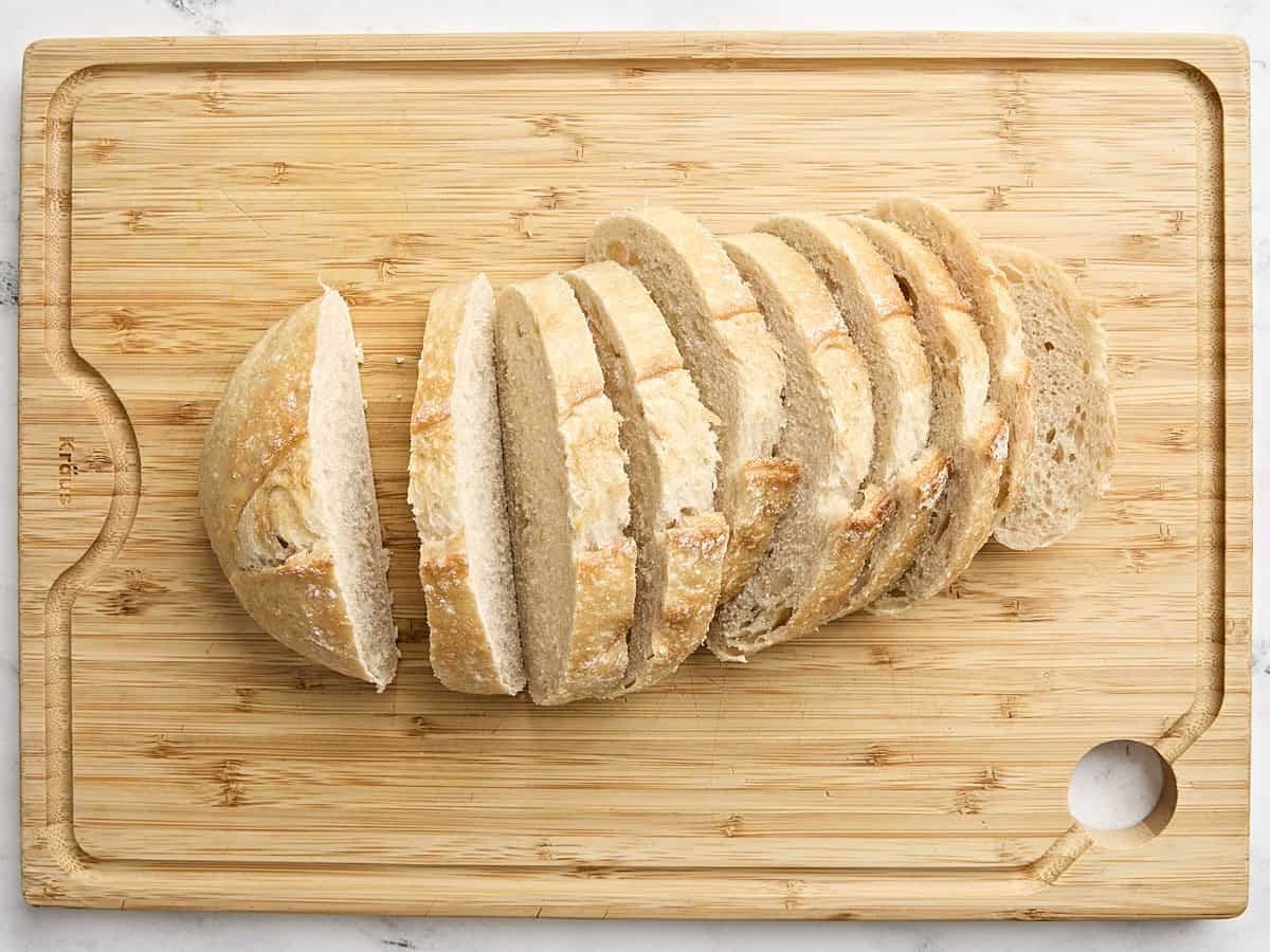 Une miche de pain au levain coupée en tranches sur une planche à découper en bois.