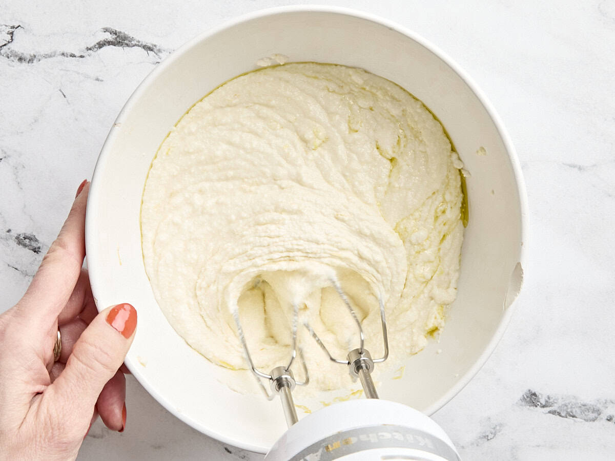 Un batteur à main fouettant la ricotta dans un bol à mélanger.