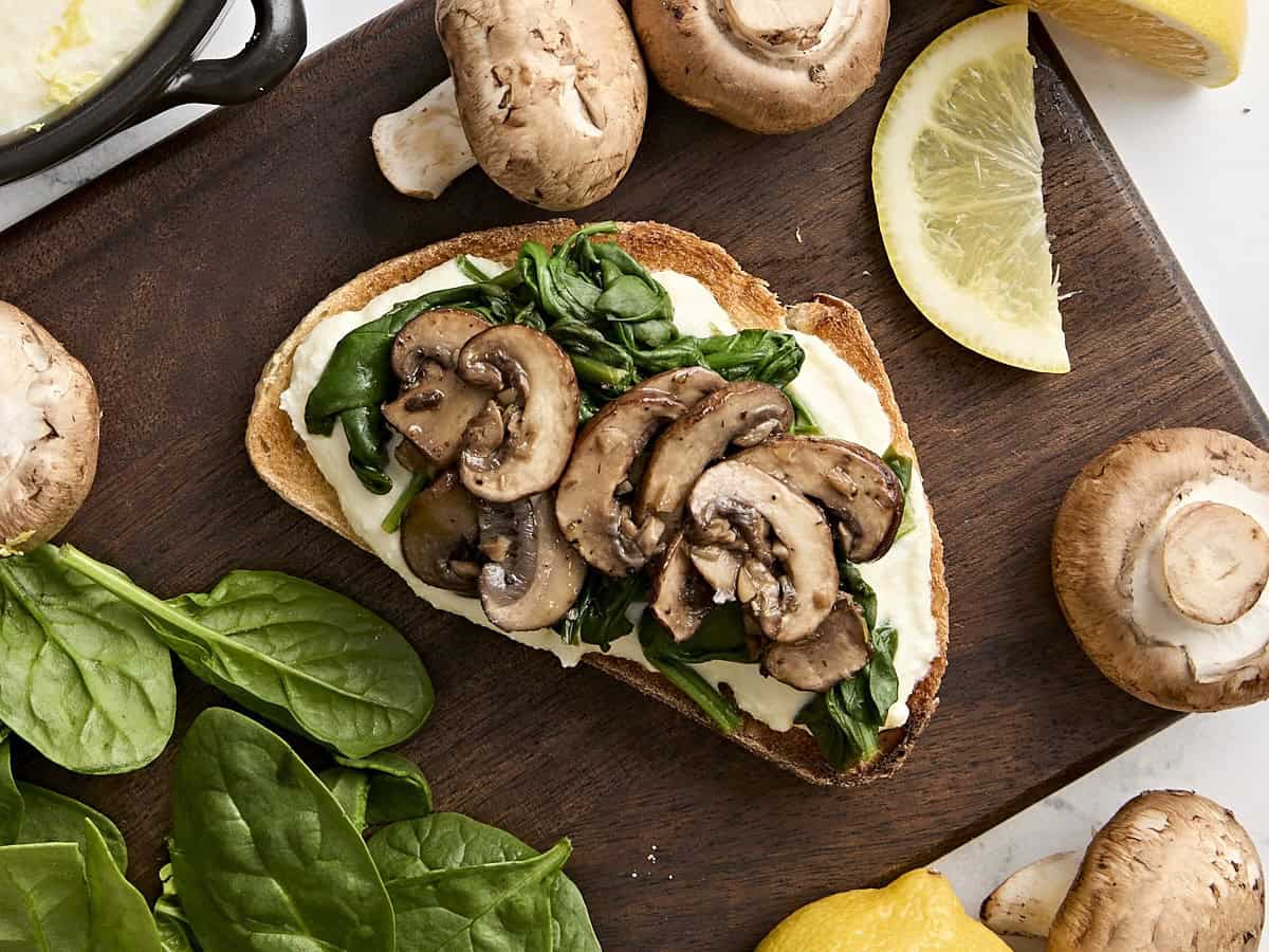 Vue aérienne du pain grillé à la ricotta avec champignons, ail, épinards fanés et poivron rouge.