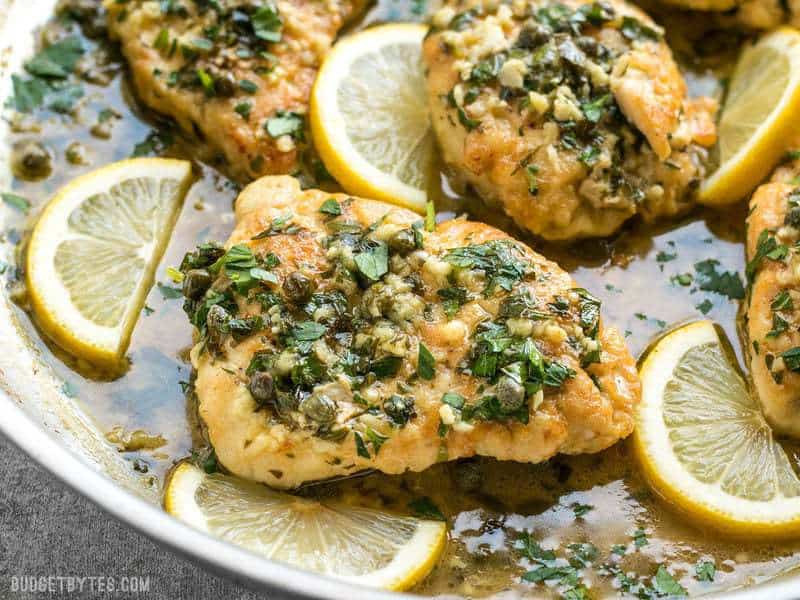 Gros plan de câpres et de persil sur un morceau de poulet piccata avec une sauce citron-ail.