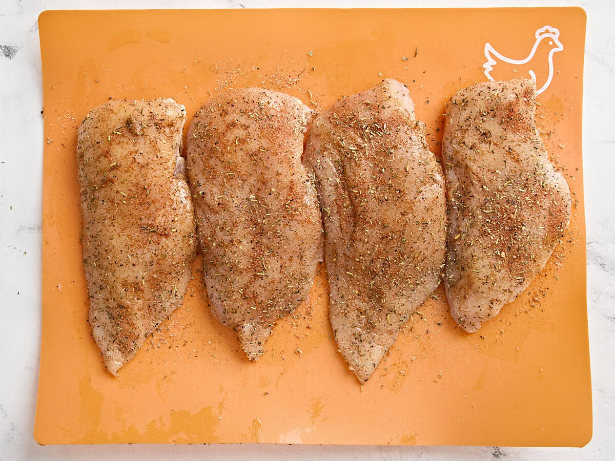 Poitrines de poulet assaisonnées sur un tapis de préparation de viande.