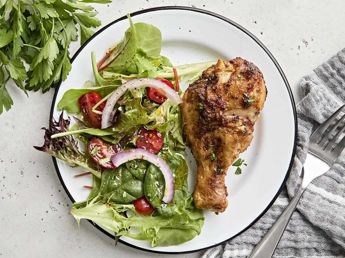 Vue aérienne d'un pilon de poulet de friteuse à air sur une assiette avec une simple salade d'accompagnement.