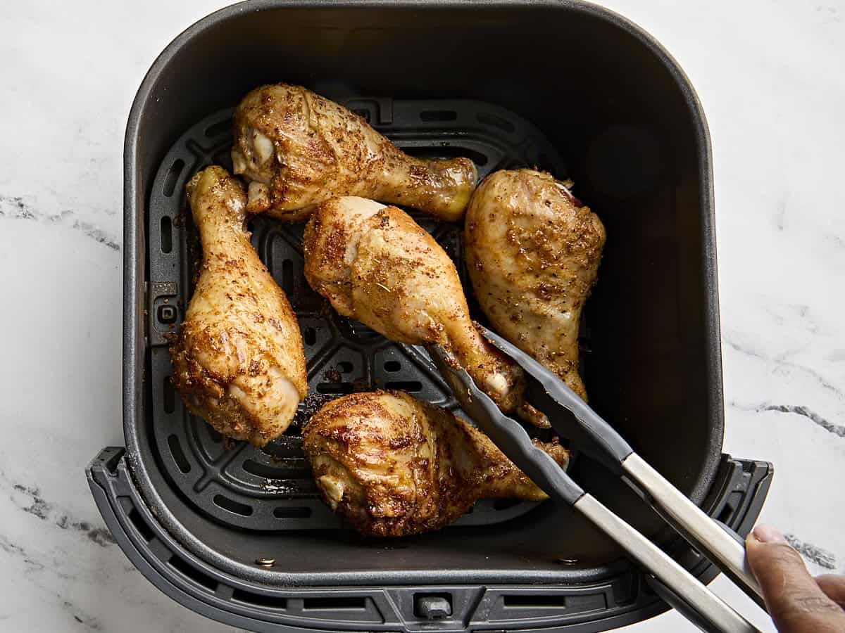Cuisson des pilons de poulet dans une friteuse à air, avec une pince en retournant un à mi-cuisson.