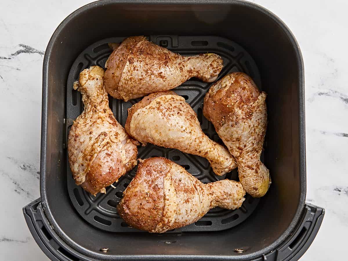 Pilons de poulet assaisonnés disposés dans un panier de friteuse à air.