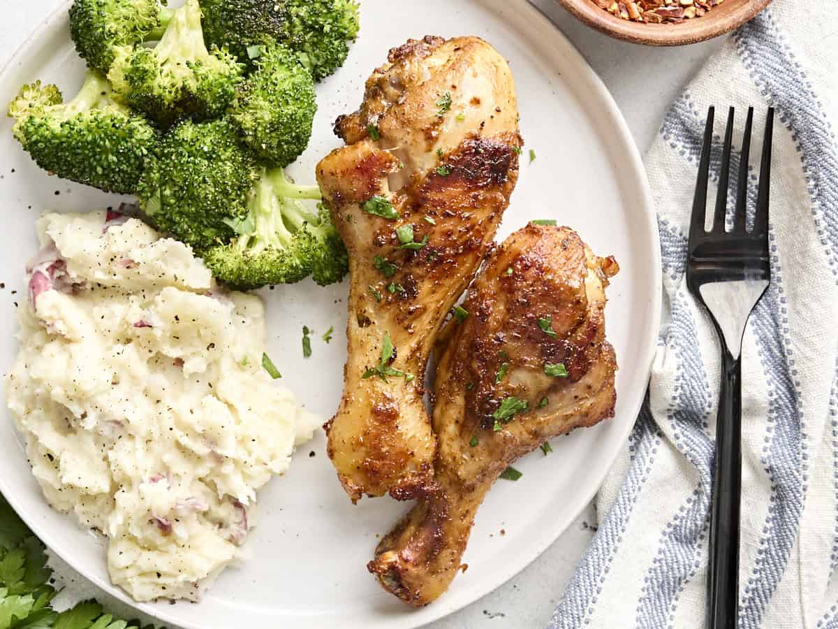 Vue rapprochée de deux pilons de poulet cuits au four sur une assiette avec du brocoli et de la purée de pommes de terre.