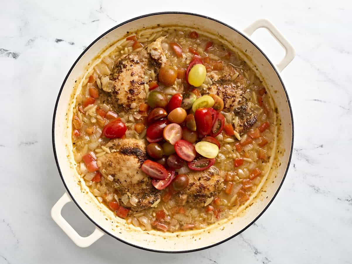 Trancher des tomates de raisin ajoutées à une poêle de poulet grec et d'orzo.