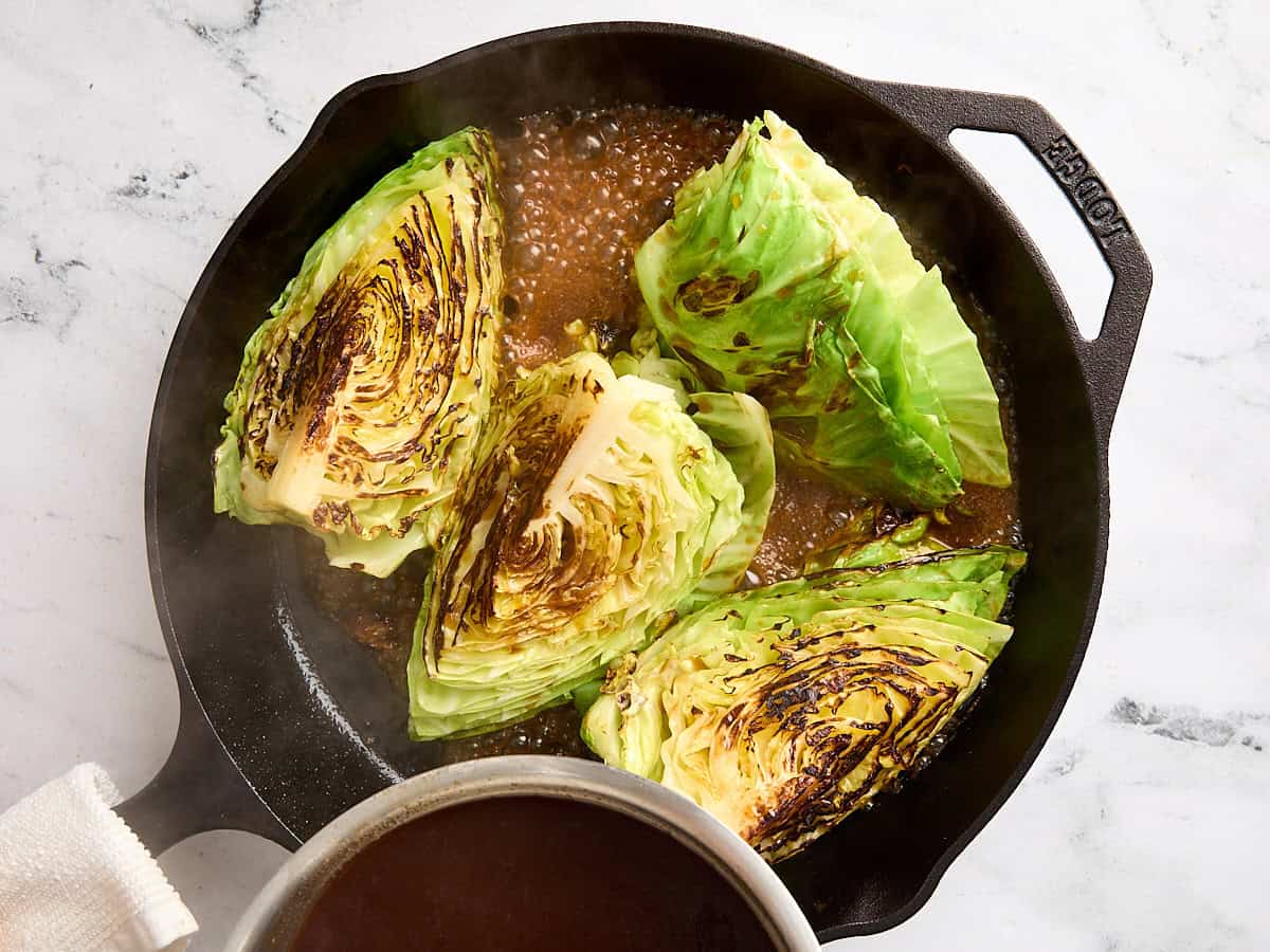 Une sauce versée sur des steaks de chou pochés dans une poêle en fonte.