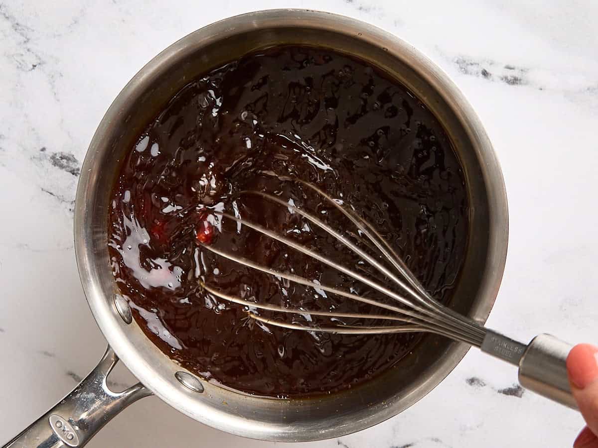 Un fouet mélangeant une sauce pour les steaks de chou dans une casserole.