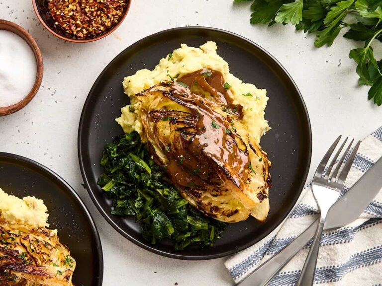 Overhead view of cabbage steaks on a plate with mashed potatoes, greens, and gravy.