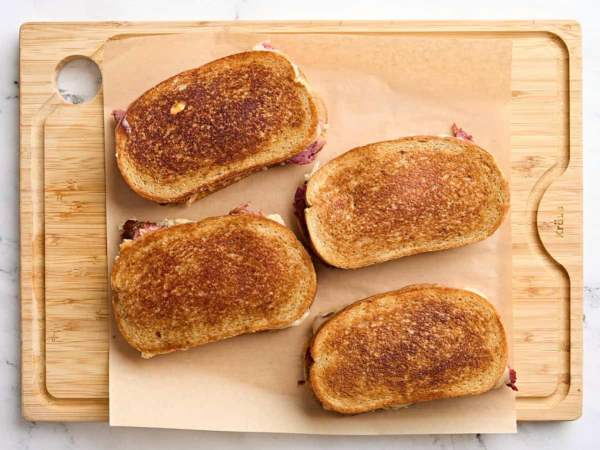 Quatre sandwichs Reuben faits maison sur une planche à découper.