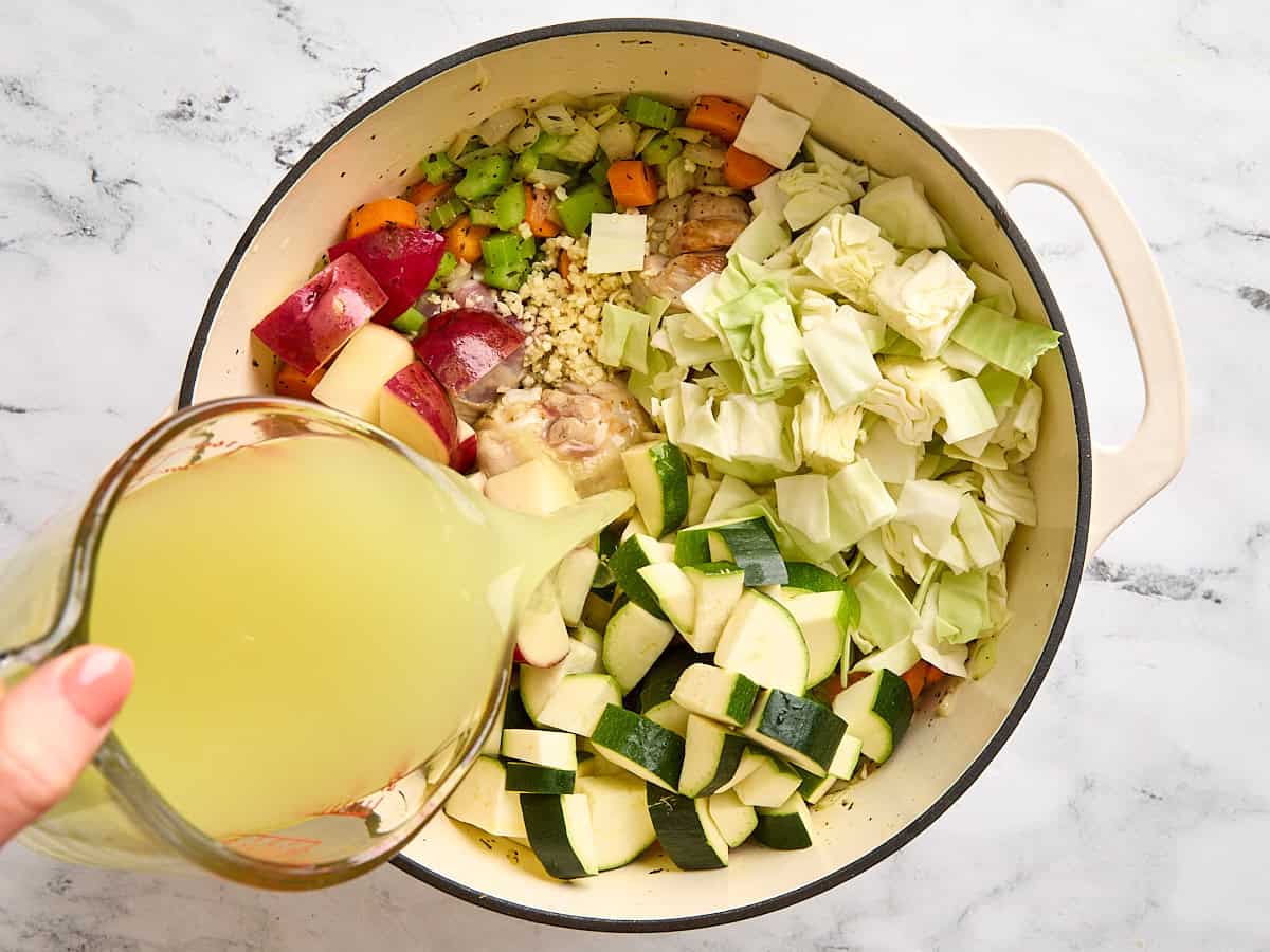 Le chou, les courgettes, les pommes de terre rouges et l'ail hachés ajoutés à un pot de bouton.