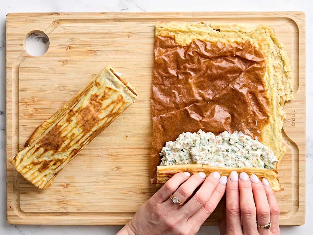 Une main enroulant une enveloppe de fromage cottage avec garniture.