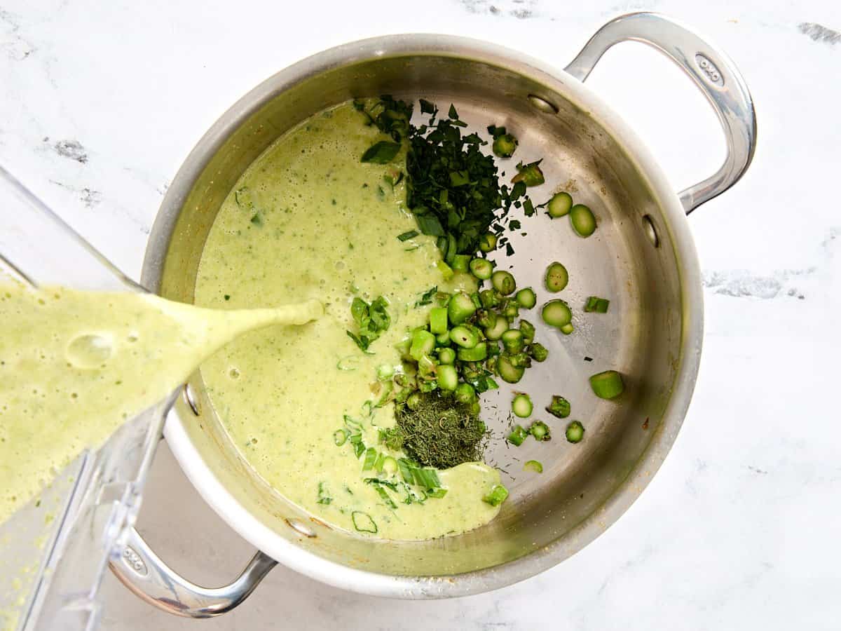 Une soupe d'asperges maison mélangée est ajoutée à une sauce avec des asperges en tranches, l'oignon vert et le persil.