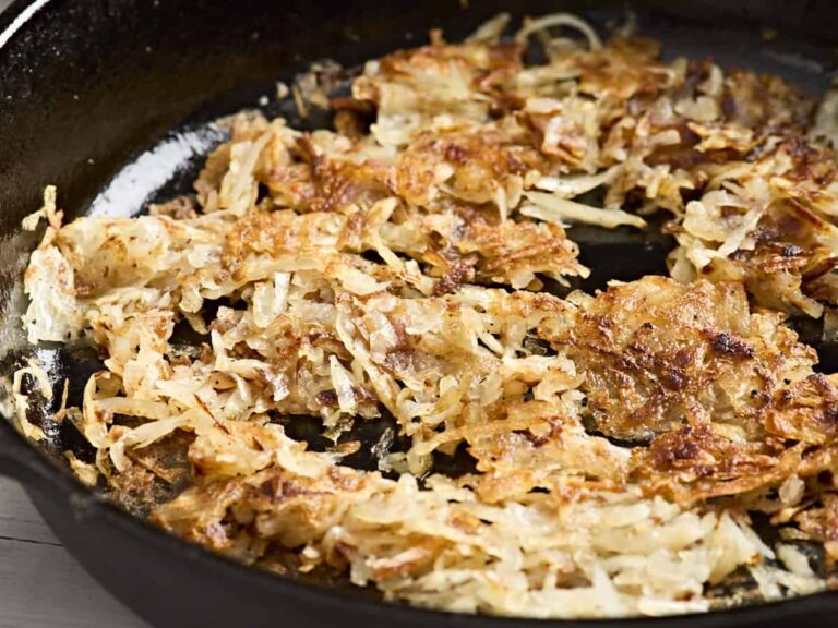 Side view close up of crispy hashbrowns cooking in a skillet.