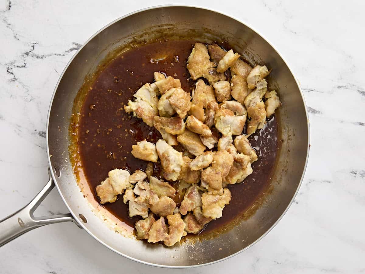 Poulet cuit ajouté à la sauce orange dans une poêle.