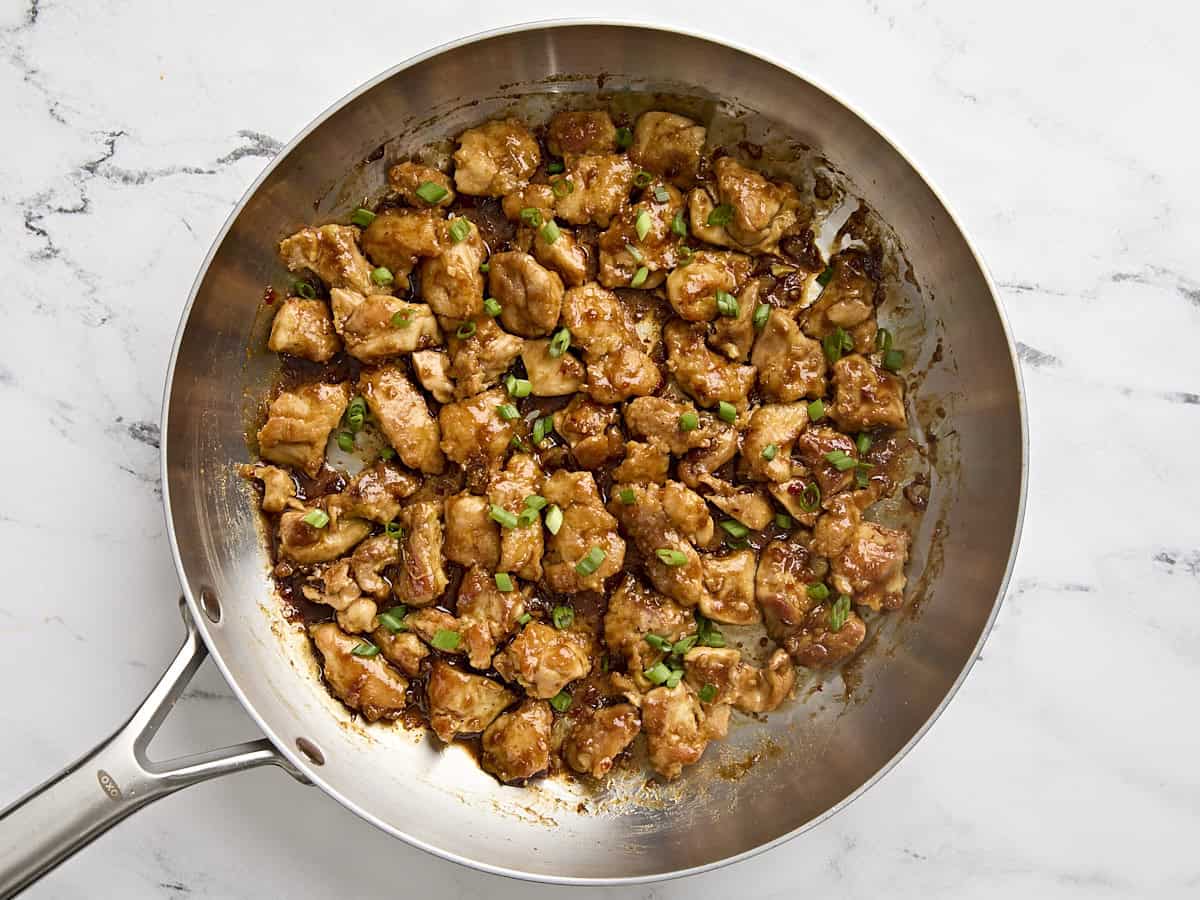 Poulet orange fini dans une poêle, garni d'oignons verts en tranches.
