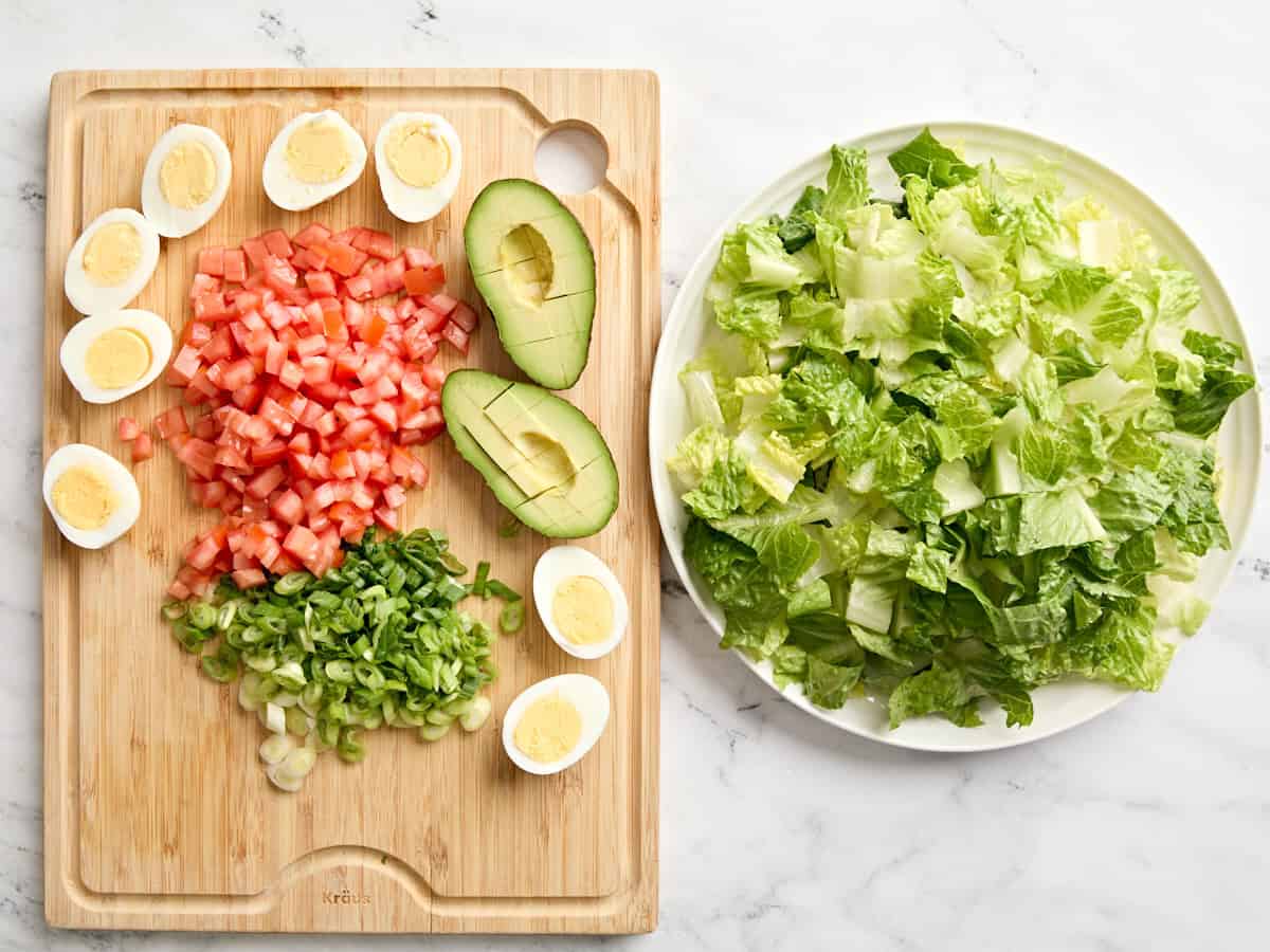 Ingrédients de salade Cobb hachés sur une planche à découper et dans un bol.