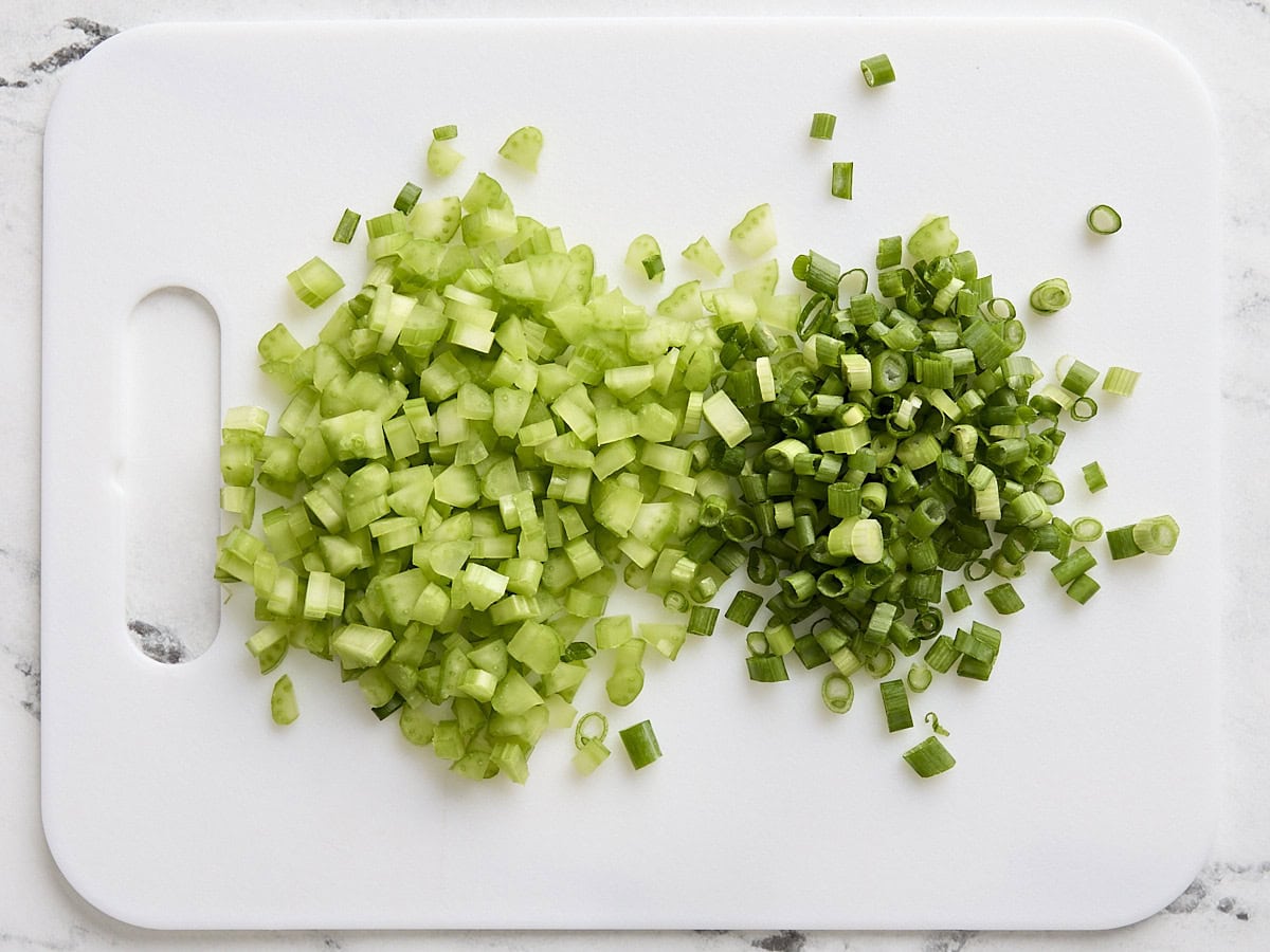 Céleri en dés et oignons verts sur une planche à découper.