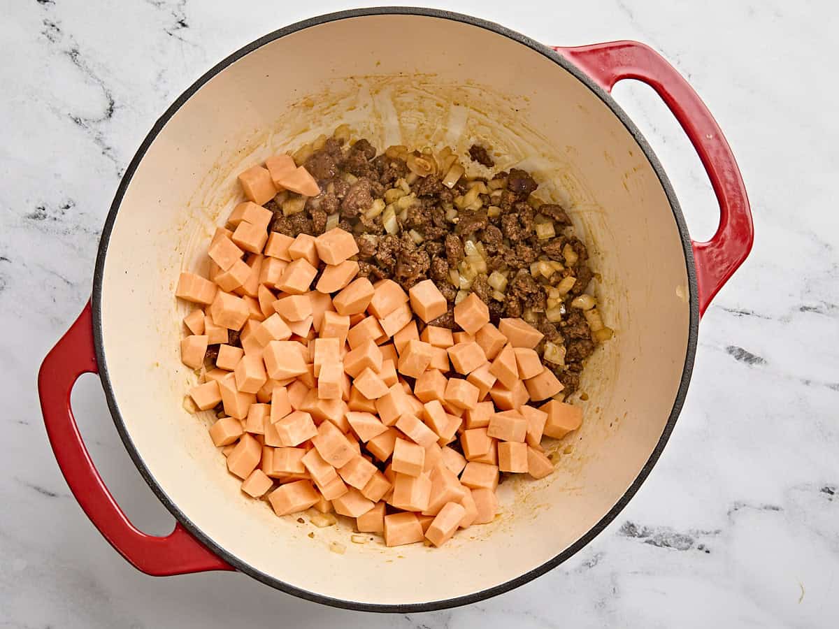 La patate douce en dés ajoutée au chorizo ​​cuit et aux oignons dans un pot.