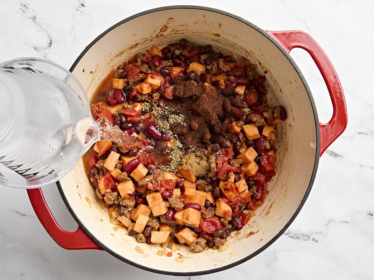 Les assaisonnements et l'eau sont ajoutés au piment de patates douces chorizo ​​dans un pot.