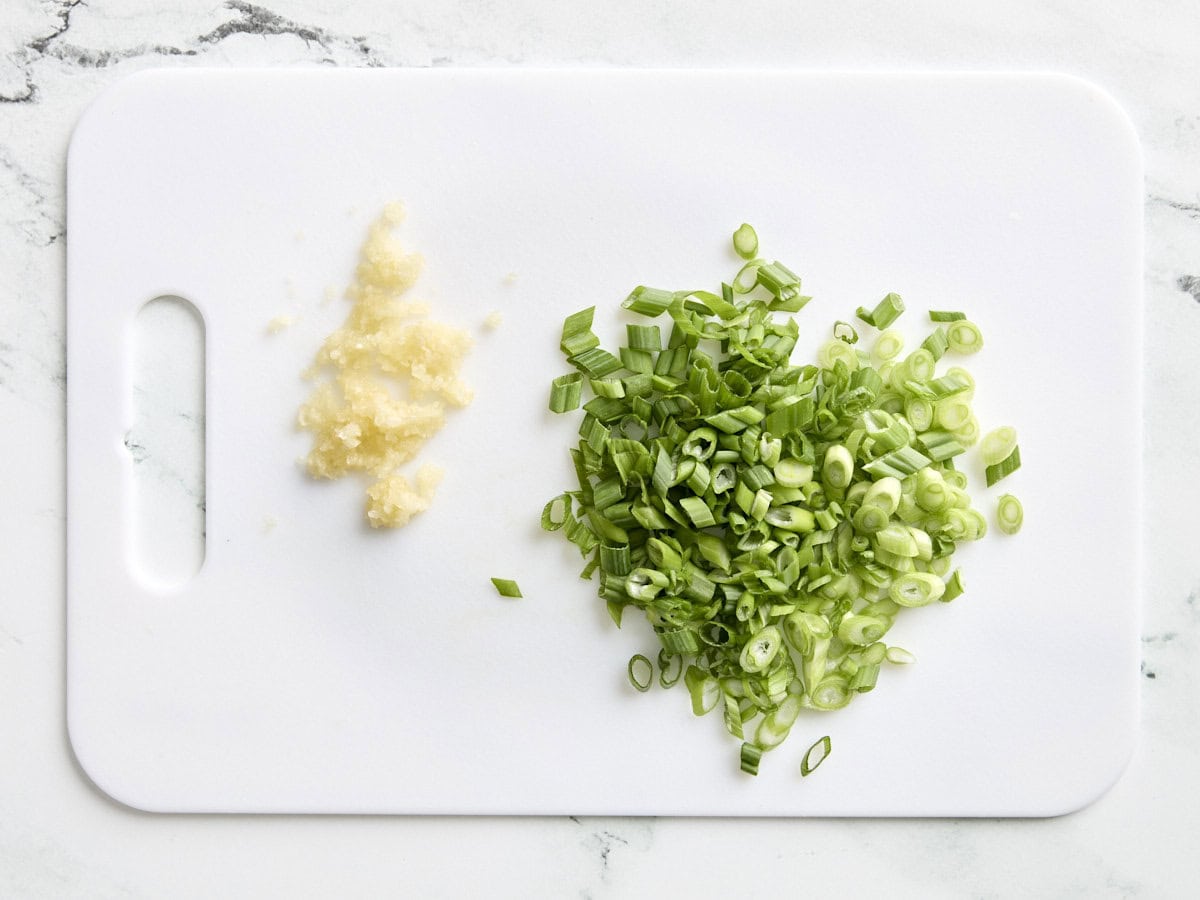 Oignons verts en dés et ail haché sur une planche à découper.