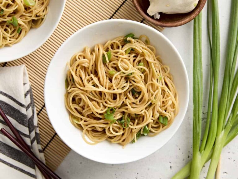 Overhead view of easy garlic noodles in a bowl, topped with sliced green onions.
