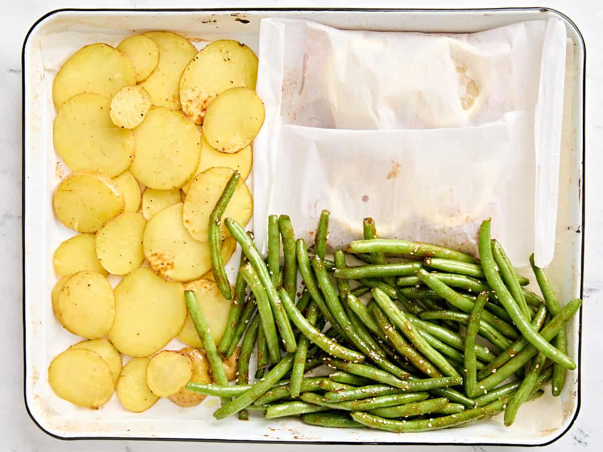 Les pommes de terre en tranches, les haricots verts et le papier parchemin ont enveloppé des filets de saumon sur une plaque à pâtisserie.