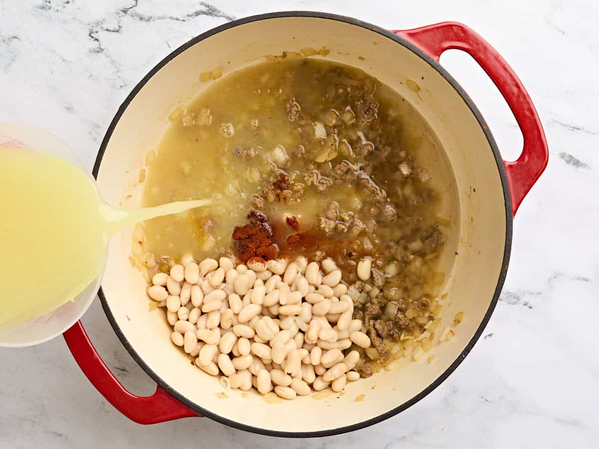 Les grands haricots du nord, le paprika fumé et le bouillon de poulet ont ajouté à une marmite avec une saucisse hachée et des oignons sautés.