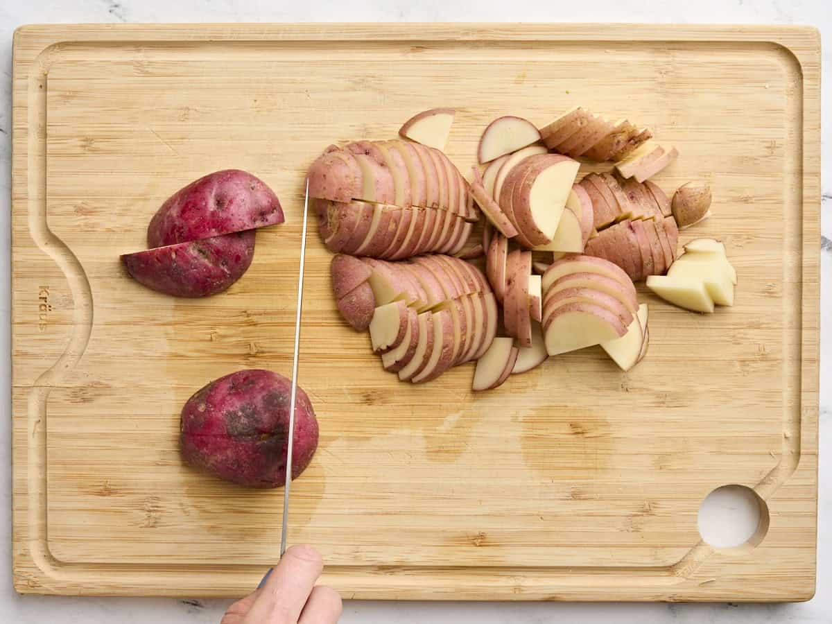 Une main tranchant des pommes de terre sur une planche à découper en bois.