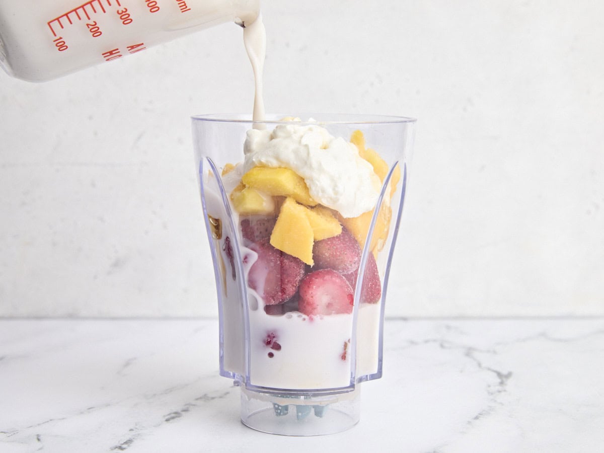 Les ingrédients pour faire un smoothie à la mangue de fraise dans un mélangeur, le lait d'amande versé.