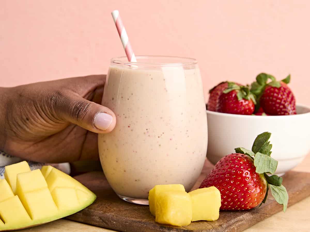 Une main tient un verre de smoothie à la mangue aux fraises.