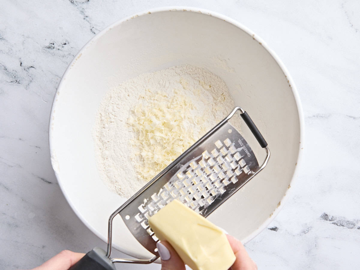 Le beurre est râpé dans un bol à mélanger de farine, de levure chimique, de sucre et de sel.