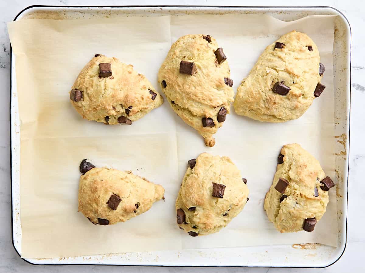 Des scones à pépites de levain fraîchement cuits sur une plaque à pâtisserie doublée de parchemin.