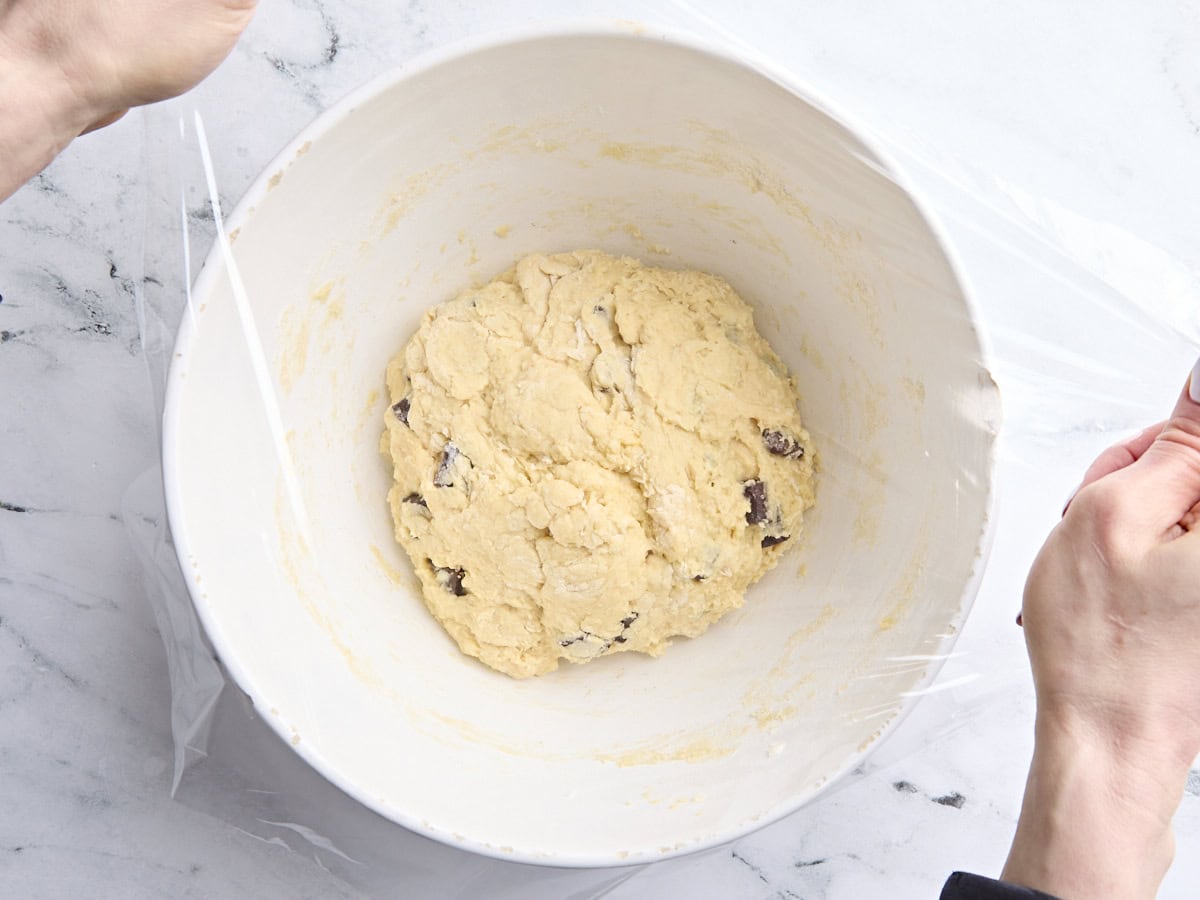 Pâte à ciel de levain aux pépites de chocolat dans un bol à mélanger, recouverte d'une pellicule plastique.