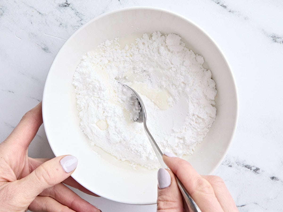 Sucre en poudre et lait dans un bol à mélanger, mélangé à une cuillère pour faire un glaçage.