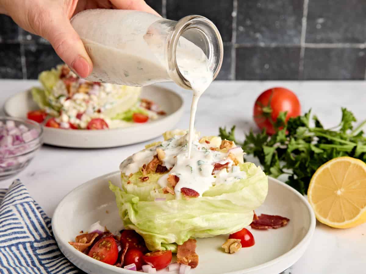 Side view of a bottle of blue cheese dressing being poured over a wedge salad.