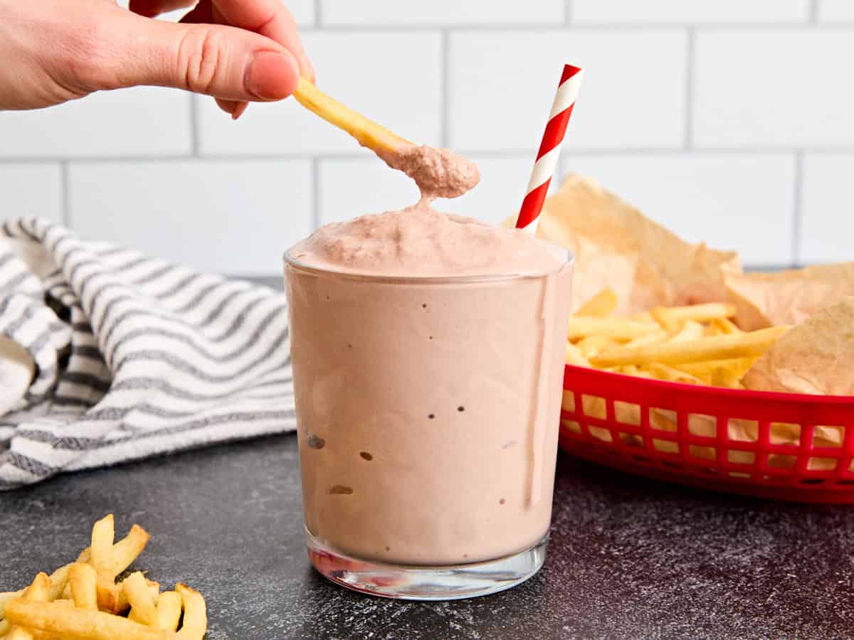 Une main qui plongeait une frite dans un verre de glacial fait maison.