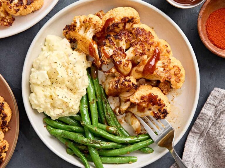 Overhead view of cauliflower steak on a plate with mashed potatoes and green beans.
